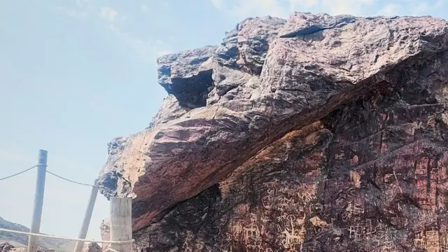 A large rust coloured boulder marked with ancient carvings, against a pale sky