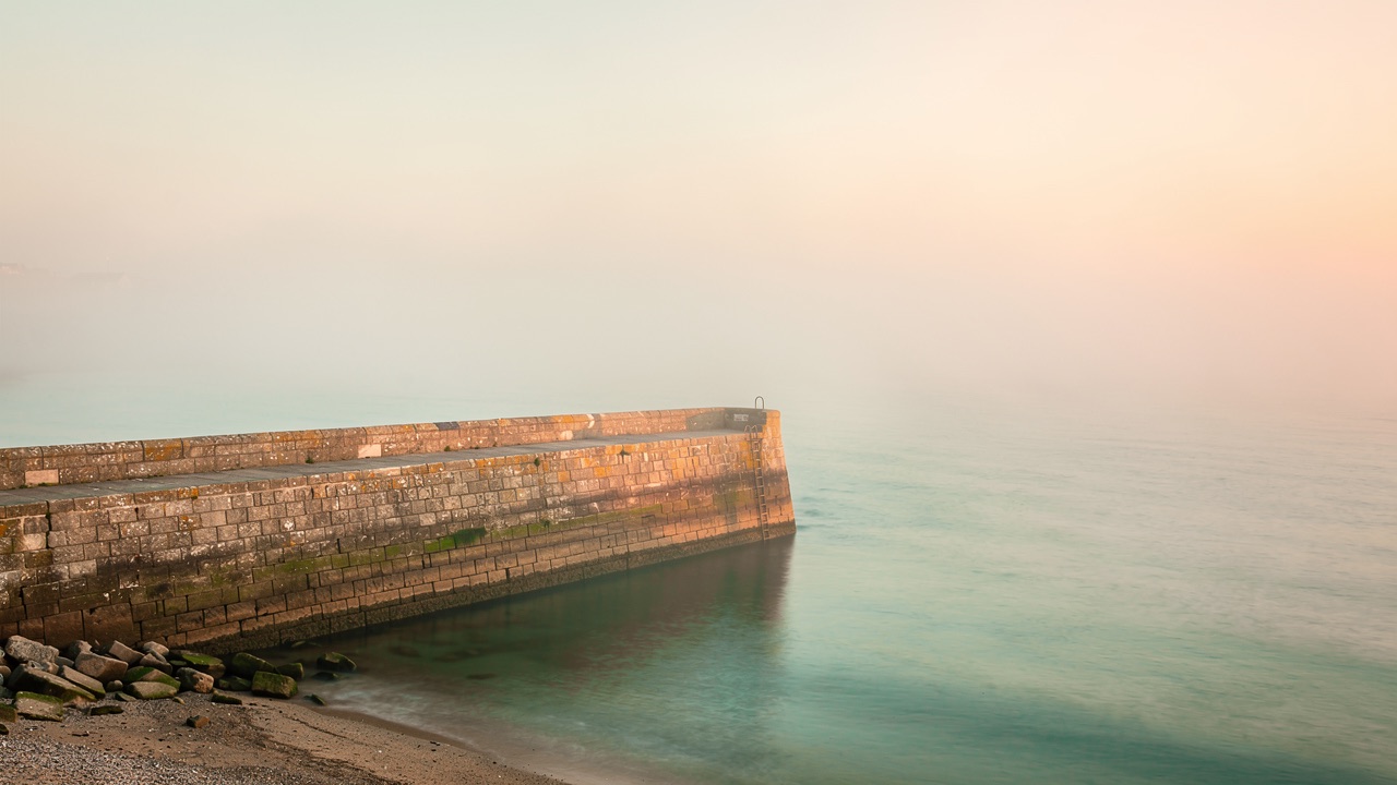 The stone harbour wall at Dunmoor fading into warm morning mist
